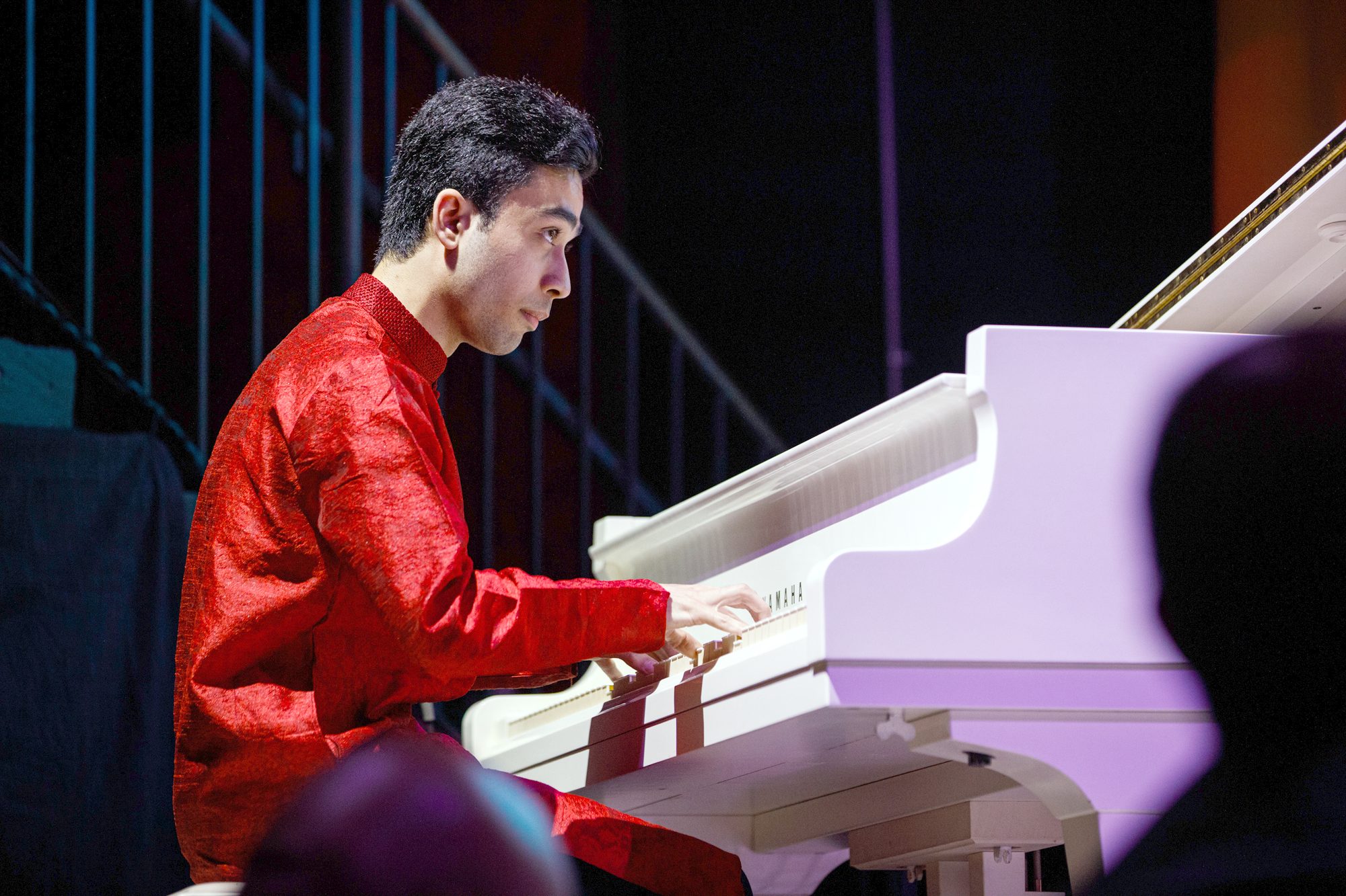 Elham Fanoos in profile, playing a white grand piano